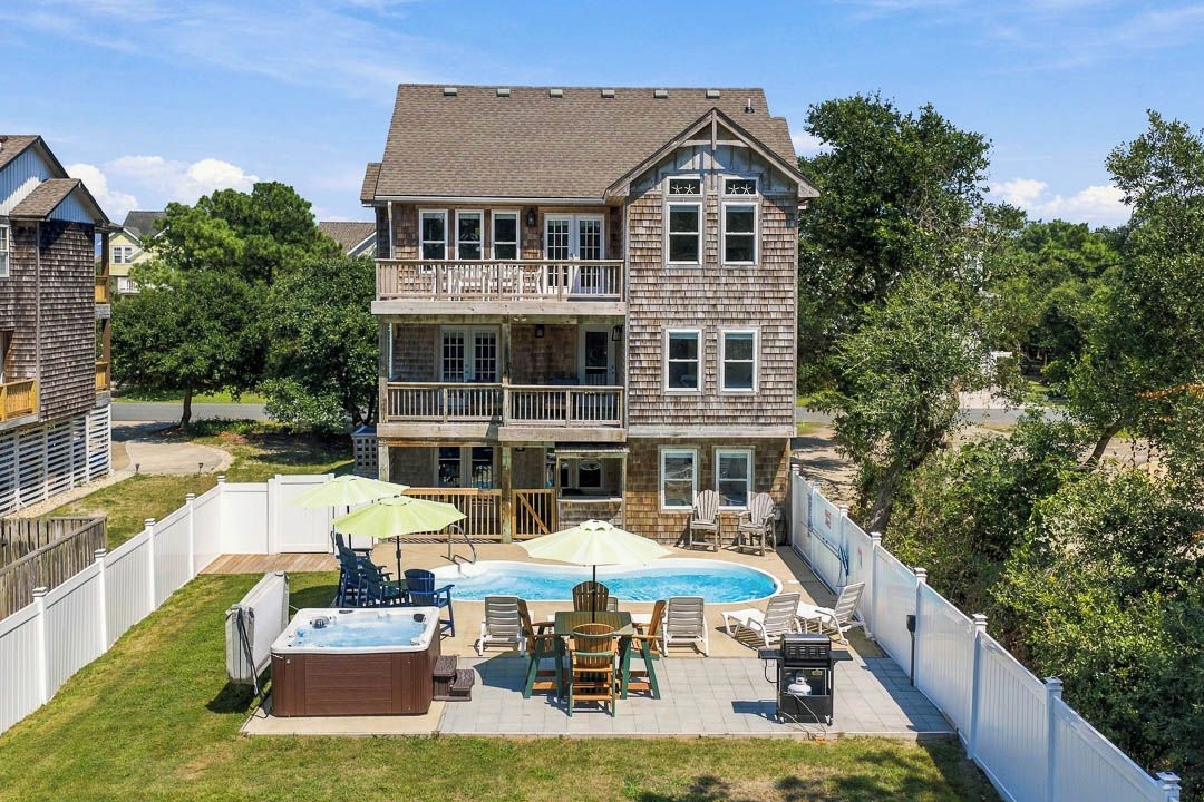 A two-story house with a backyard featuring a swimming pool, hot tub, and outdoor seating area.