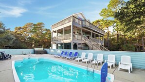 Piscina com espreguiçadeiras e um edifício de dois andares com varanda.