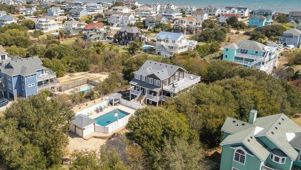 Oversigtsbillede af et kystnære boligområde med huse, en swimmingpool og en strand.