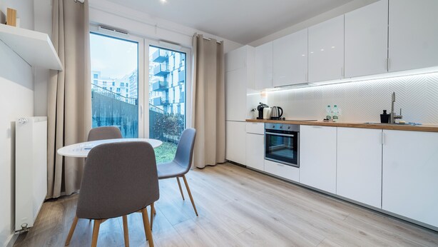 A modern kitchen with white cabinets, a built-in oven, and a window overlooking a cityscape. - Jeżyce Apartment with Garden (Poznań)