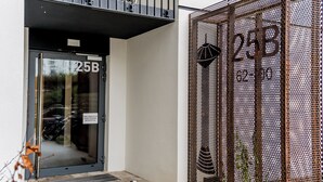 En bygningseingang med en glasdør, hvor der står "25B", og et metalhegn med dekorative detaljer.