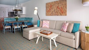 A living room with a sofa, coffee table, and chairs. There is a kitchen area with cabinets and a refrigerator. A decorative wall piece is visible. - Resort Getaway Ideal for Families, Disney Trips & Relaxation (Orlando)