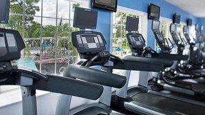 A row of treadmills with digital displays, a large window with a view of trees and a building, and a blue wall. - Resort Getaway Ideal for Families, Disney Trips & Relaxation (Orlando)