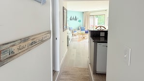 A hallway leading to a dining area with a view of the outdoors, a kitchen with a black countertop, and a sign on the wall that reads 'BEACH'. - 222 Mariner's Court - Steps from the Boardwalk, Beach, Dining & Everything Rehoboth Has to Offer! (Rehoboth Beach)