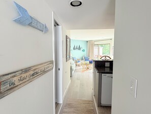 A hallway leading to a dining area with a view of the outdoors, a kitchen with a black countertop, and a sign on the wall that reads 'BEACH'. - 4 Laurel Street # 222- Mariners Court. Perfect location! Community Pool! Downtown! (Rehoboth Beach)