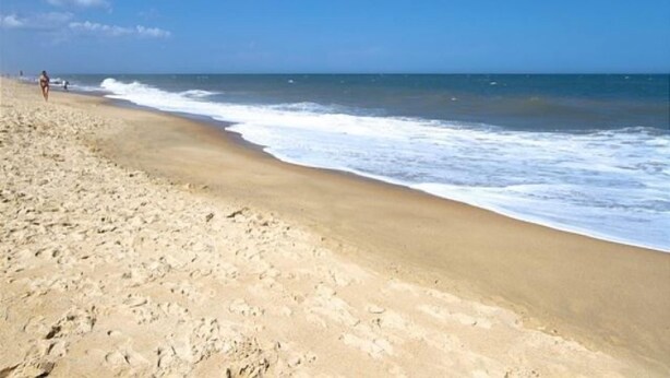 A beach with footprints leading to the water, a clear sky, and a person walking in the distance. - 222 Mariner's Court - Steps from the Boardwalk, Beach, Dining & Everything Rehoboth Has to Offer! (Rehoboth Beach)