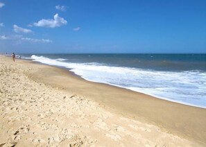Una spiaggia con impronte che conducono all'acqua, cielo sereno e una persona che cammina in lontananza.