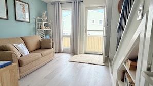 A living room with a sofa, a glass cabinet, and a staircase. - 222 Mariner's Court - Steps from the Boardwalk, Beach, Dining & Everything Rehoboth Has to Offer! (Rehoboth Beach)