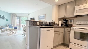 A modern kitchen with a dishwasher, oven, and microwave. There is a dining area with chairs and a table. - 222 Mariner's Court - Steps from the Boardwalk, Beach, Dining & Everything Rehoboth Has to Offer! (Rehoboth Beach)