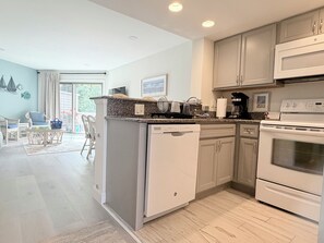 A modern kitchen with a dishwasher, oven, and microwave. There is a dining area with chairs and a table. - 4 Laurel Street # 222- Mariners Court. Perfect location! Community Pool! Downtown! (Rehoboth Beach)