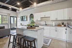 A modern kitchen with white cabinets, a granite countertop, and a central island with stools. - 1BR Condo - King Bed - 10mins to Broadway (Nashville)
