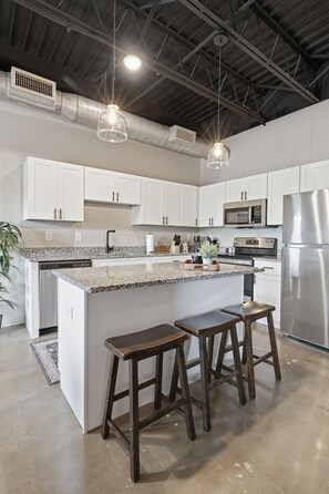 A modern kitchen with white cabinets, stainless steel appliances, and a central island with stools. - 1BR Condo - King Bed - 10mins to Broadway (Nashville)