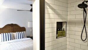 A hotel room with a bed, a nightstand, a wall-mounted mirror, and a shower area with a handheld showerhead. - Birchfrost cottage | Quintessential cosy | Central Orange (Orange)
