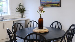 A dining area with a round table, six chairs, and a vase with flowers. - Birchfrost cottage | Quintessential cosy | Central Orange (Orange)