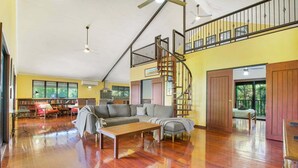 Amplia sala de estar con piso de madera, un conjunto de sofás, una mesa de comedor y una escalera que conduce a un nivel superior.