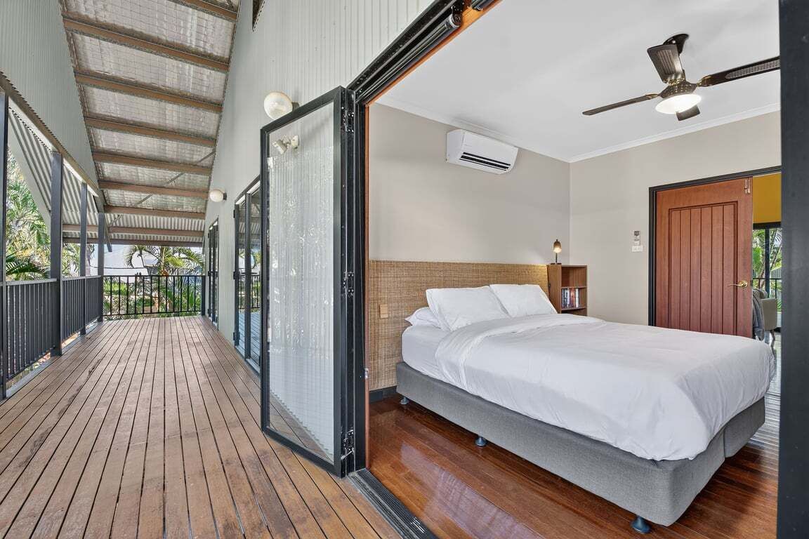 A bedroom with a bed, a ceiling fan, an air conditioning unit, and a view through a glass door to an outdoor area.