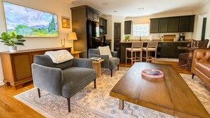 Una sala de estar moderna con un sofá gris, una mesa de centro de madera, y una zona de cocina con armarios oscuros y una ventana.