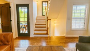Un salón amplio con suelo de madera, una escalera y una puerta que da a un patio.