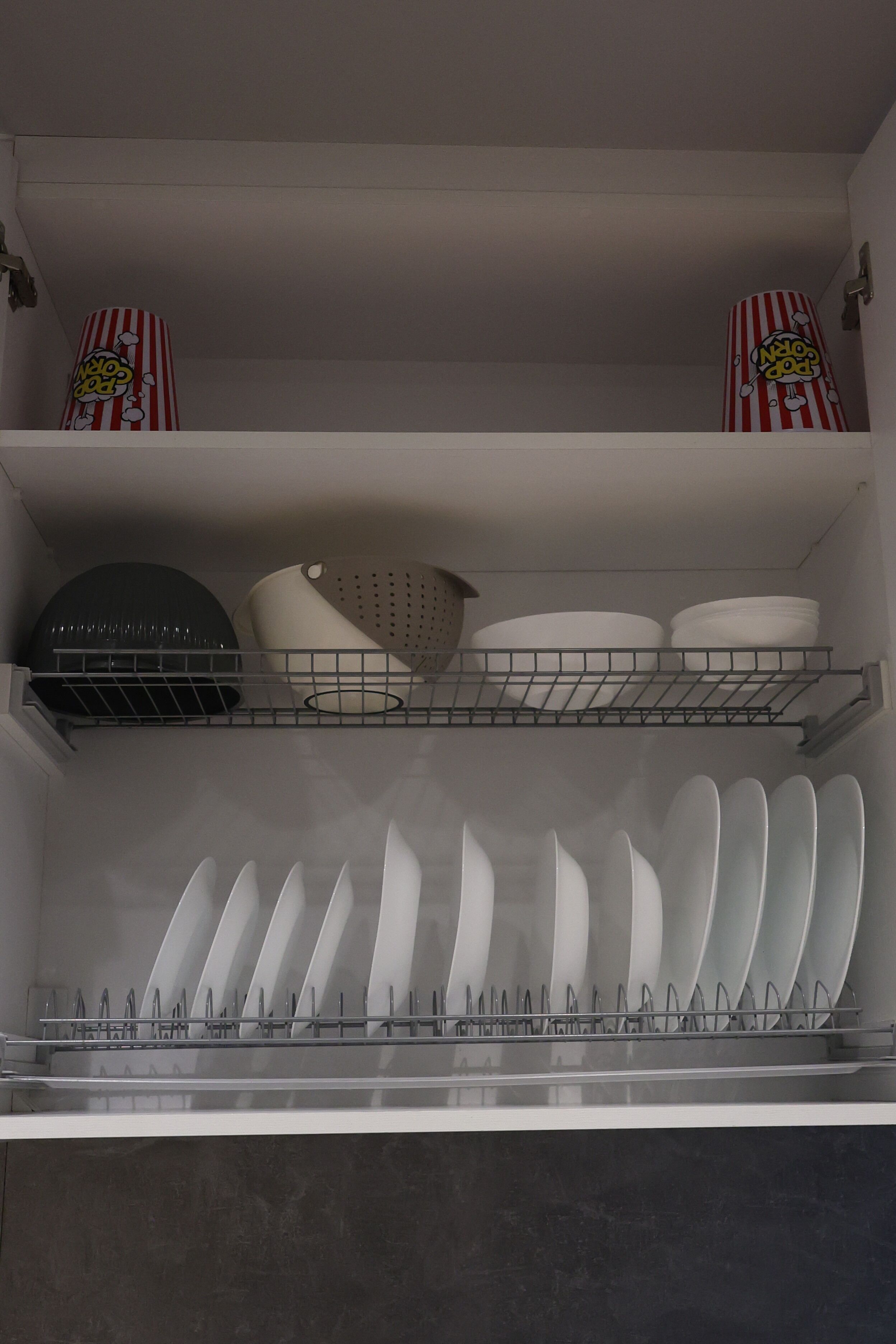 Een keuken met witte kastjes, een afwasschaal en een plank met decoratieve spullen.