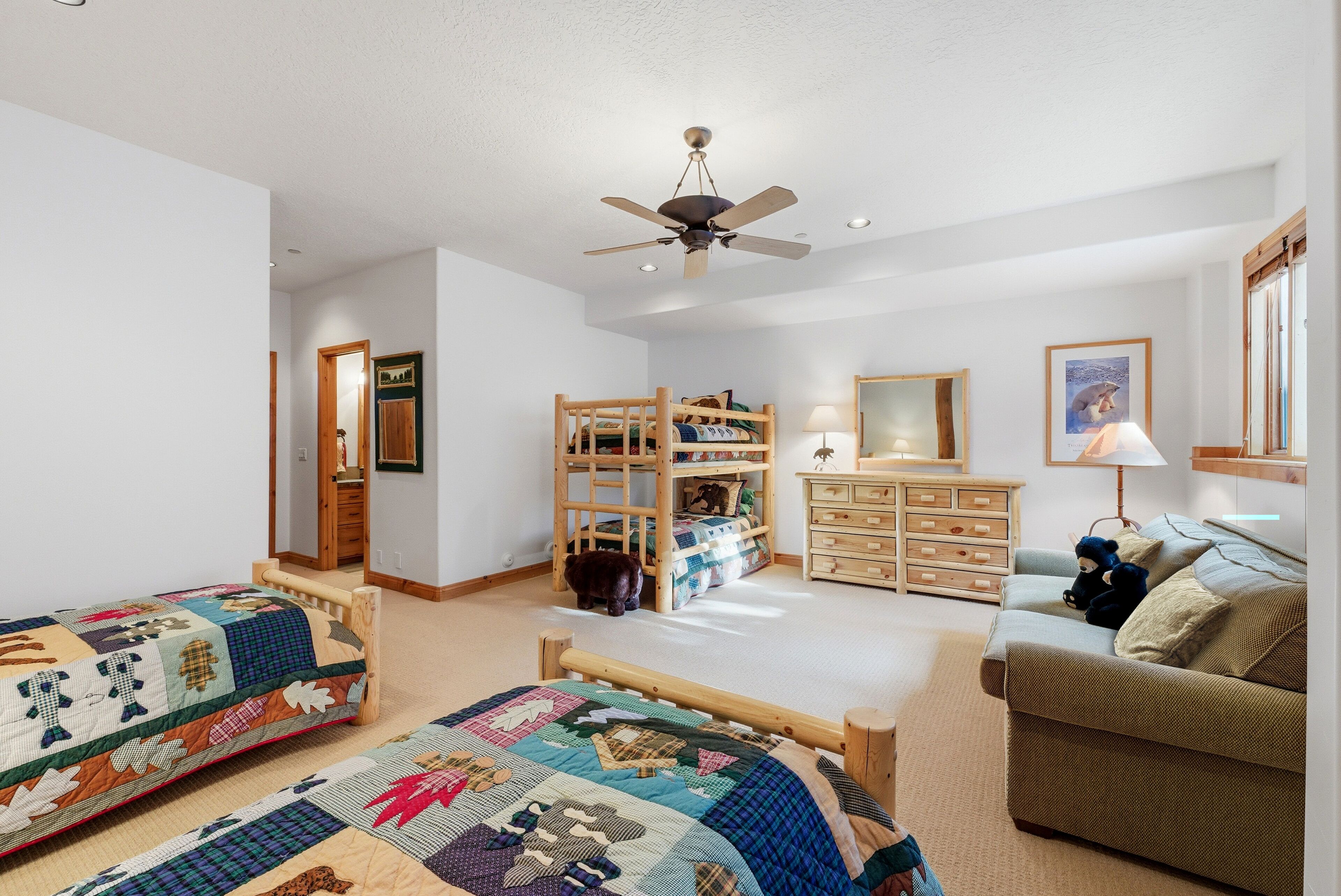 A child’s bedroom with bunk beds, a ceiling fan, a dresser, and a couch.