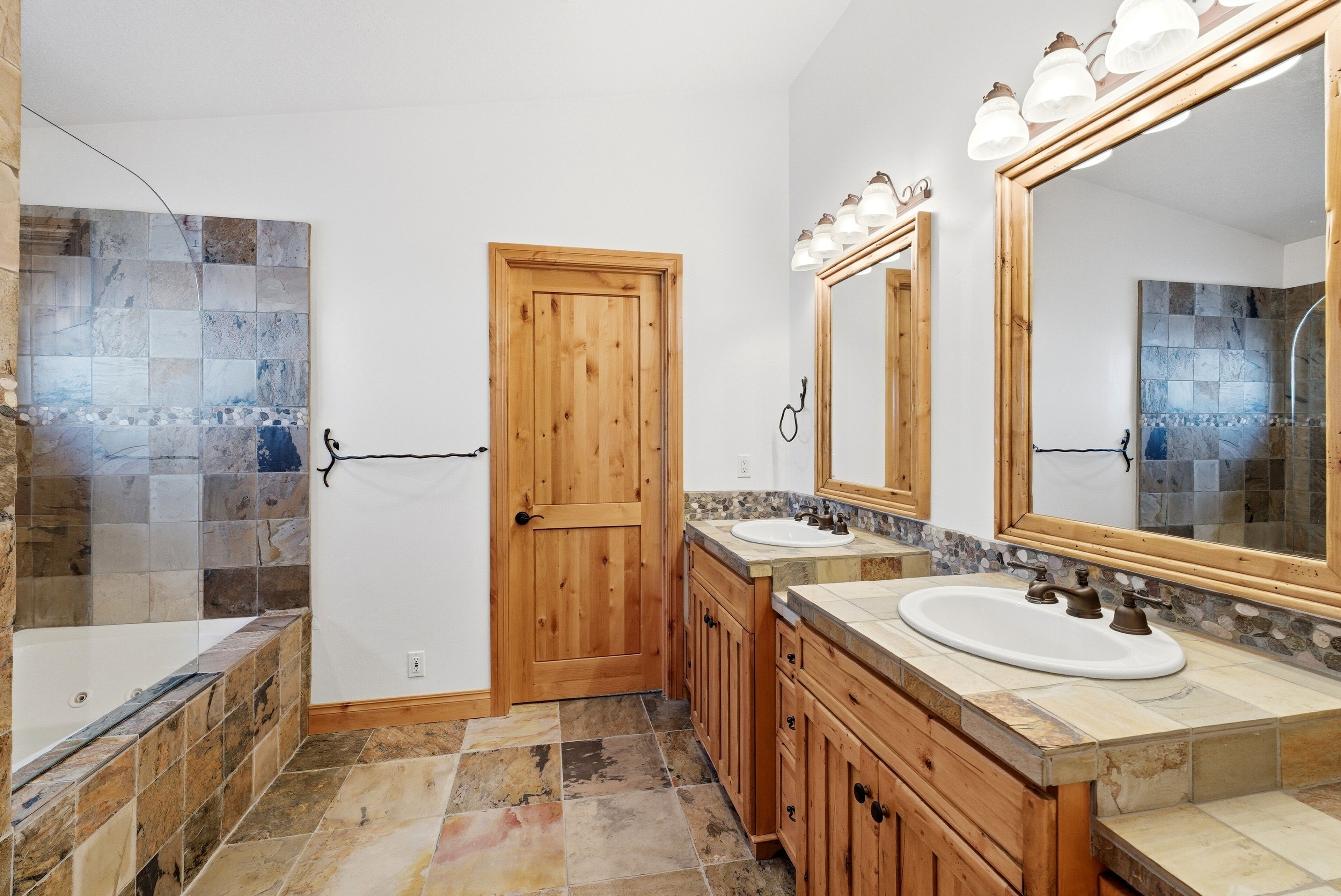 A bathroom with a wooden door, two sinks, a large mirror, and a shower area.