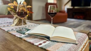 An open book on a wooden table with two wine glasses, a woven placemat, and a vase with flowers. - Yough Lake Streamside Cottage w/ Hot Tub, Pavilion, Firepit (Confluence)