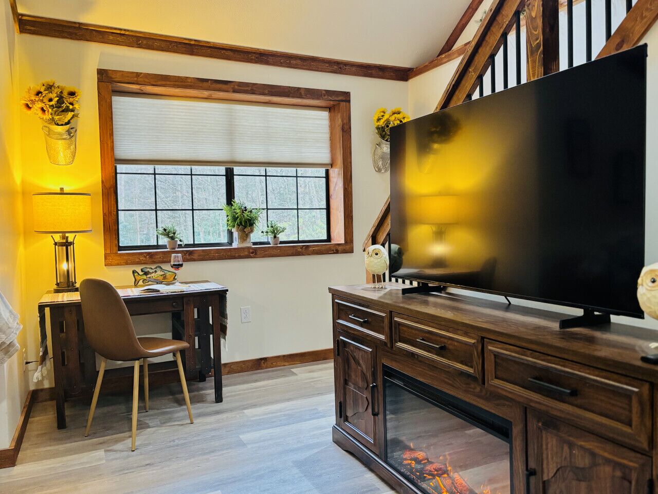 A living room with a large flat-screen TV, wooden furniture, a fireplace, and a window with blinds.