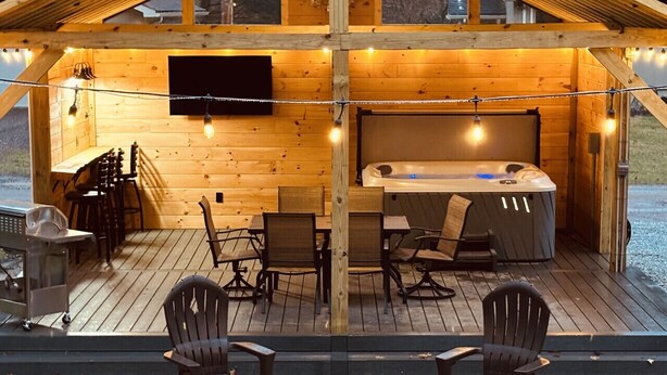 A wooden cabin with a hot tub, string lights, and outdoor seating. - Yough Lake Streamside Cottage w/ Hot Tub, Pavilion, Firepit (Confluence)
