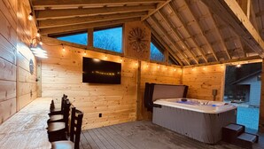 A wooden cabin with a dining table and chairs, a hot tub, and a TV mounted on the wall. - Yough Lake Streamside Cottage w/ Hot Tub, Pavilion, Firepit (Confluence)