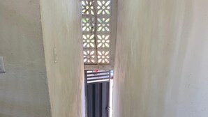 Um corredor estreito, com um banco de madeira à esquerda, piso de azulejos e uma porta no final.