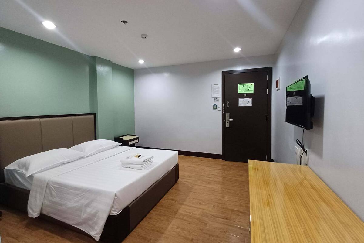 A hotel room with a bed, bedside table, and a TV mounted on the wall.