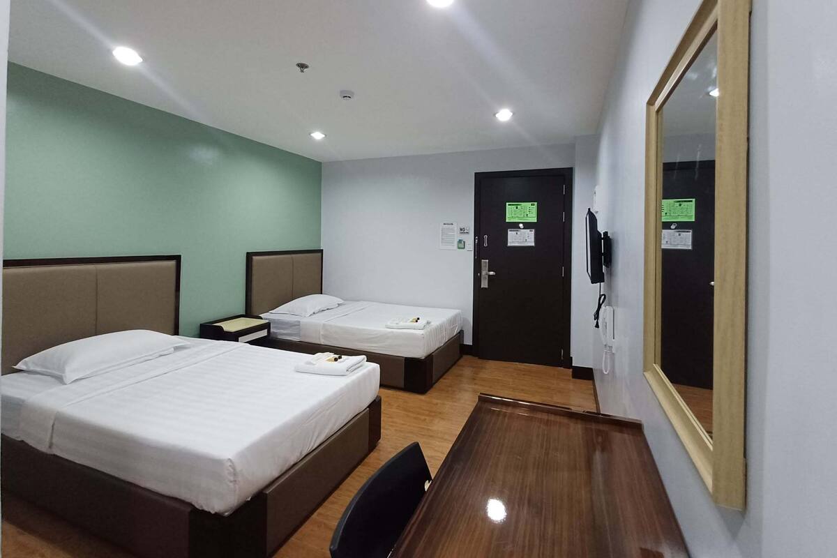 A hotel room with two beds, a wooden desk, a mirror, and a door with a phone and a sign.