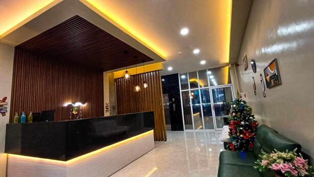 A modern reception area with a wooden reception desk, a Christmas tree, and a green sofa. - Asia Jem Hotel - Bacolod City (Bacolod)