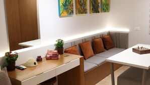 Una habitación moderna con un escritorio de madera, un sofá gris y una mesa blanca. Hay tres cuadros en la pared, una planta en el escritorio y un tablero de ajedrez en la mesa.