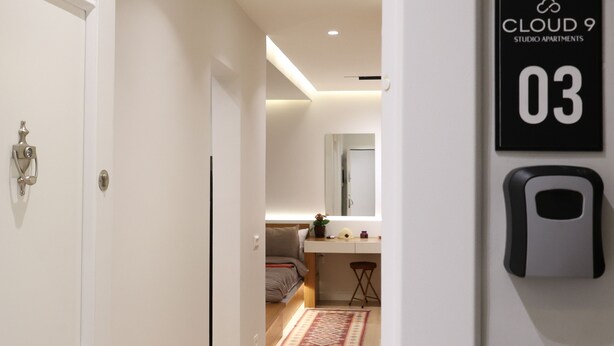Un interior moderno con una puerta blanca, una pequeña kitchenette, un espejo y un cartel que indica "CLOUD 9 STUDIO APARTMENTS 03".
