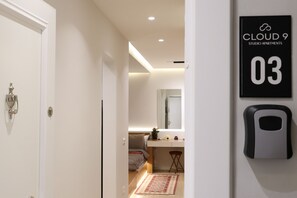 Ein modernes Interieur mit einer weißen Tür, einer kleinen Küchenzeile, einem Spiegel und einem Schild mit der Aufschrift 'CLOUD 9 STUDIO APARTMENTS 03'.