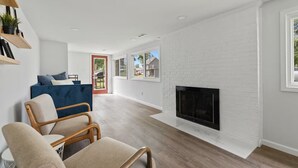 A modern living room with a fireplace, a blue sofa, and wooden flooring. - Modern & Clean Waterfront Retreat - Beach, Fire Pit, Pet friendly, Getaway (White Lake)