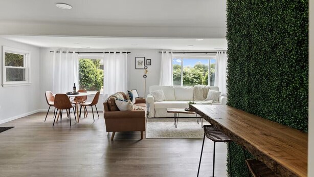 A modern living room with a wooden dining table, a sofa, and a green wall feature. - Modern & Clean Waterfront Retreat - Beach, Fire Pit, Pet friendly, Getaway (White Lake)