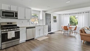 A modern kitchen with white cabinets, stainless steel appliances, and a dining area with a table and chairs. - Modern & Clean Waterfront Retreat - Beach, Fire Pit, Pet friendly, Getaway (White Lake)