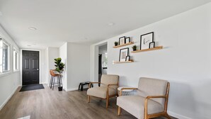 A modern living room with two beige armchairs, a wooden coffee table, and a dining area with a small table and chairs. - Modern & Clean Waterfront Retreat - Beach, Fire Pit, Pet friendly, Getaway (White Lake)