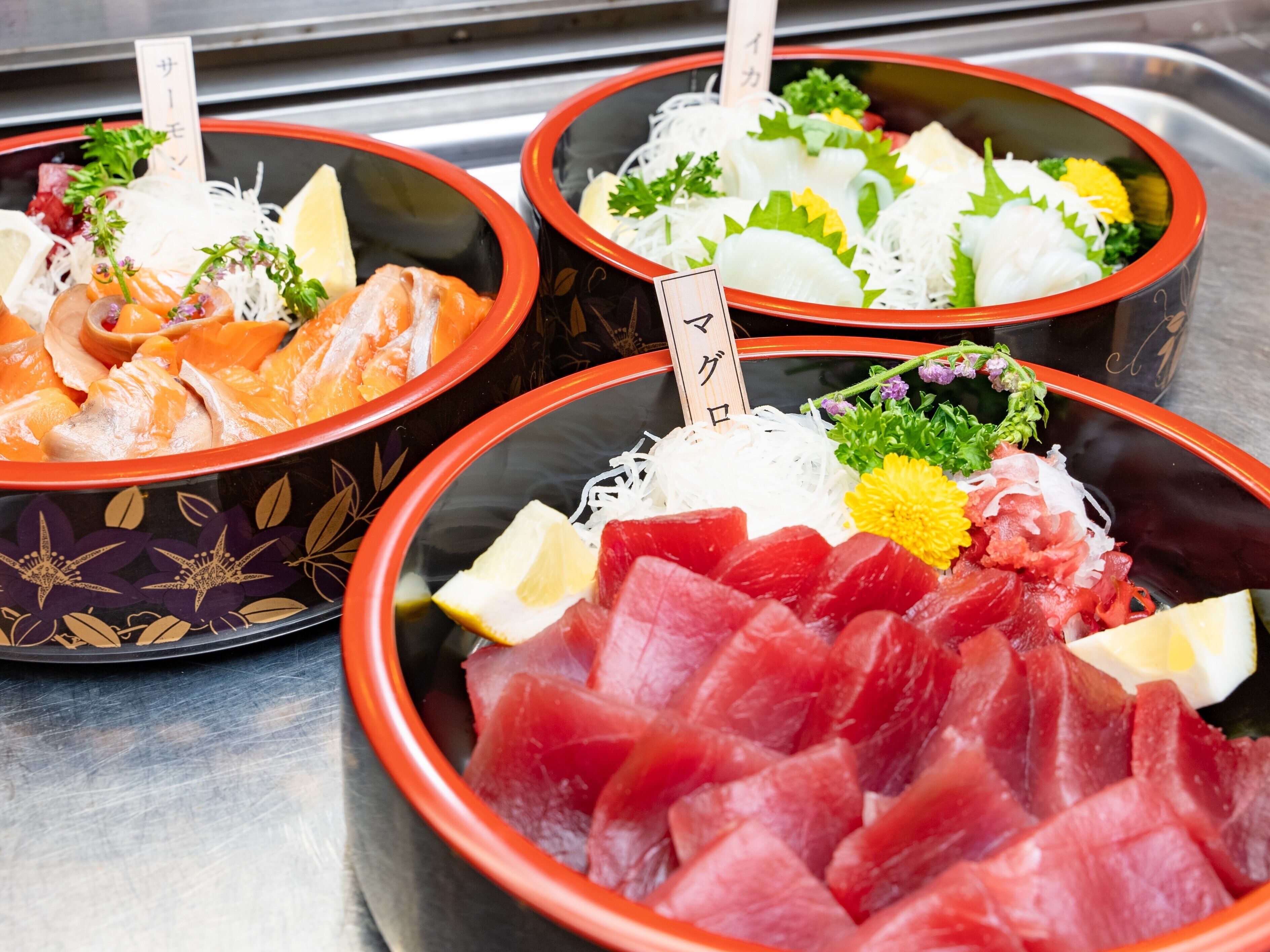 Tres porciones de sashimi con diferentes ingredientes y adornos.