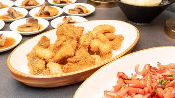 A buffet table with various dishes including breaded chicken wings, a bowl of soup, and a plate of sliced tomatoes.