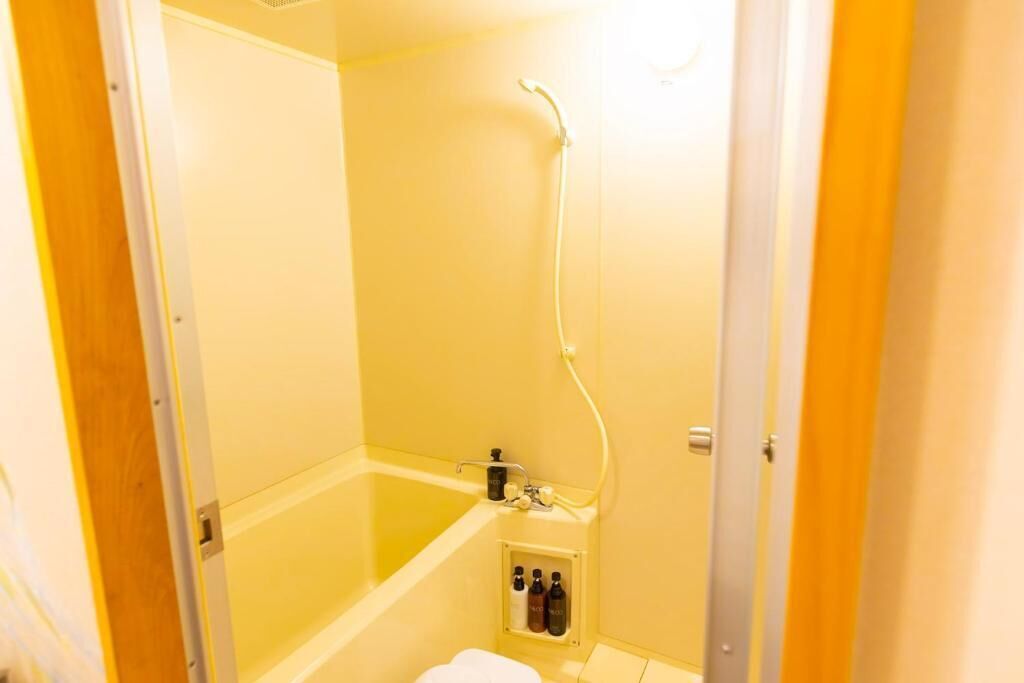 A small, enclosed bathroom with a bathtub, shower, and a shelf with toiletries.