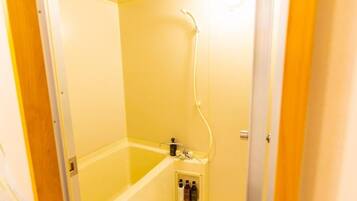 A small, enclosed bathroom with a bathtub, shower, and a shelf with toiletries.
