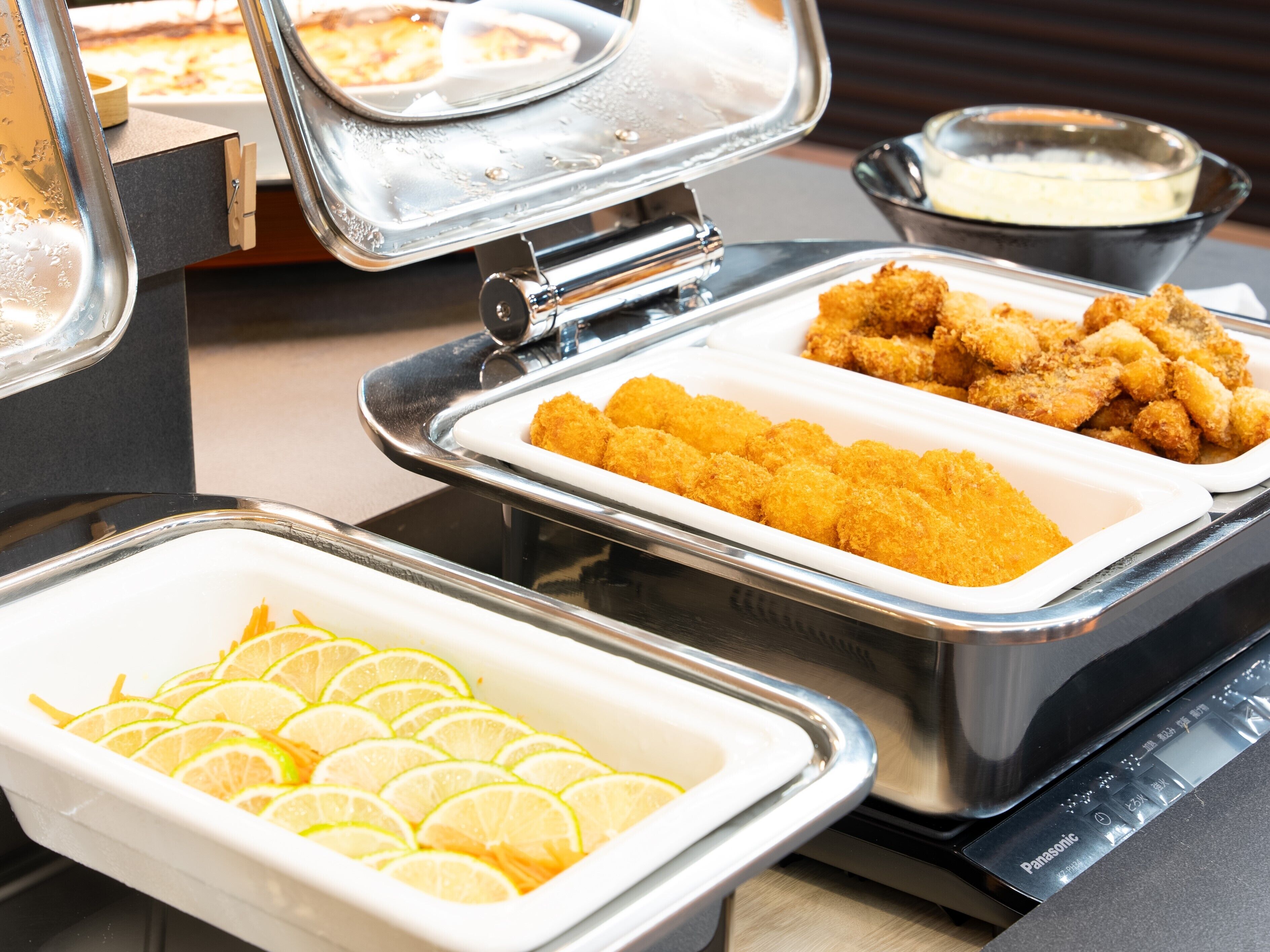 A buffet setup with various food items including breaded chicken, lemon slices, and a creamy sauce.