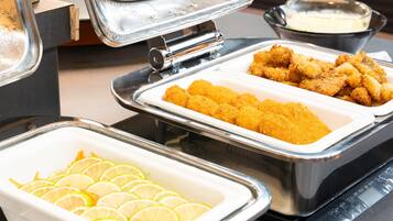 A buffet setup with various food items including breaded chicken, lemon slices, and a creamy sauce.
