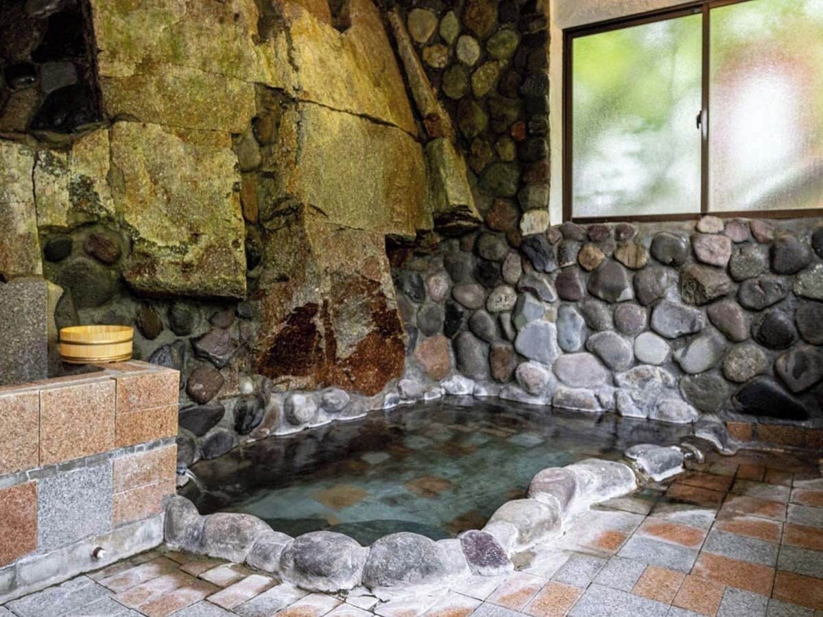 Un baño termal de paredes de piedra con un cuenco de madera y una ventana.