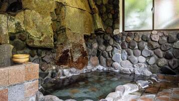 Un baño termal de paredes de piedra con un cuenco de madera y una ventana.