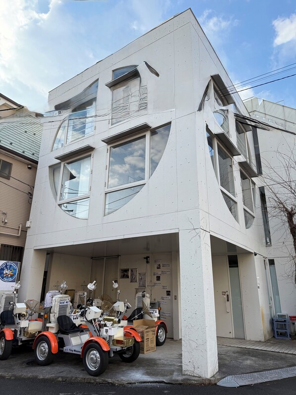 A modern building with a garage entrance, a parked vehicle, and a signboard. - Moon Base Tokyo Inn (Tokyo)