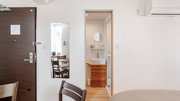 A hotel room with a wooden door, a mirror, a sink, and a bed. - Moon Base Tokyo Inn (Tokyo)